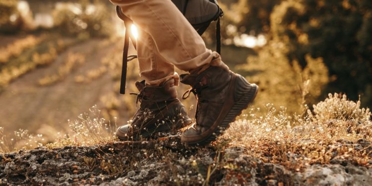 Side view of crop active male backpacker in trekking boots walking on trail in sunny summer day